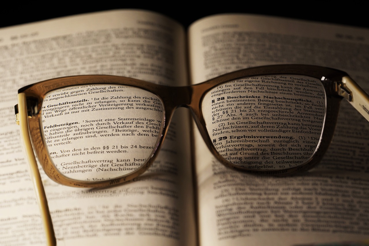 a-book-3101151_1280 EIn Buch auf dem eine Brille liegt. Die Brille fokusiert einen gesetzestext